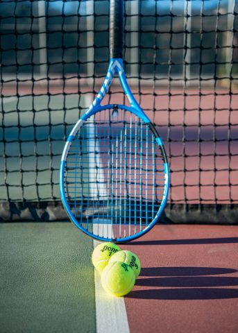 racket and tennis balls next to net on tennis court